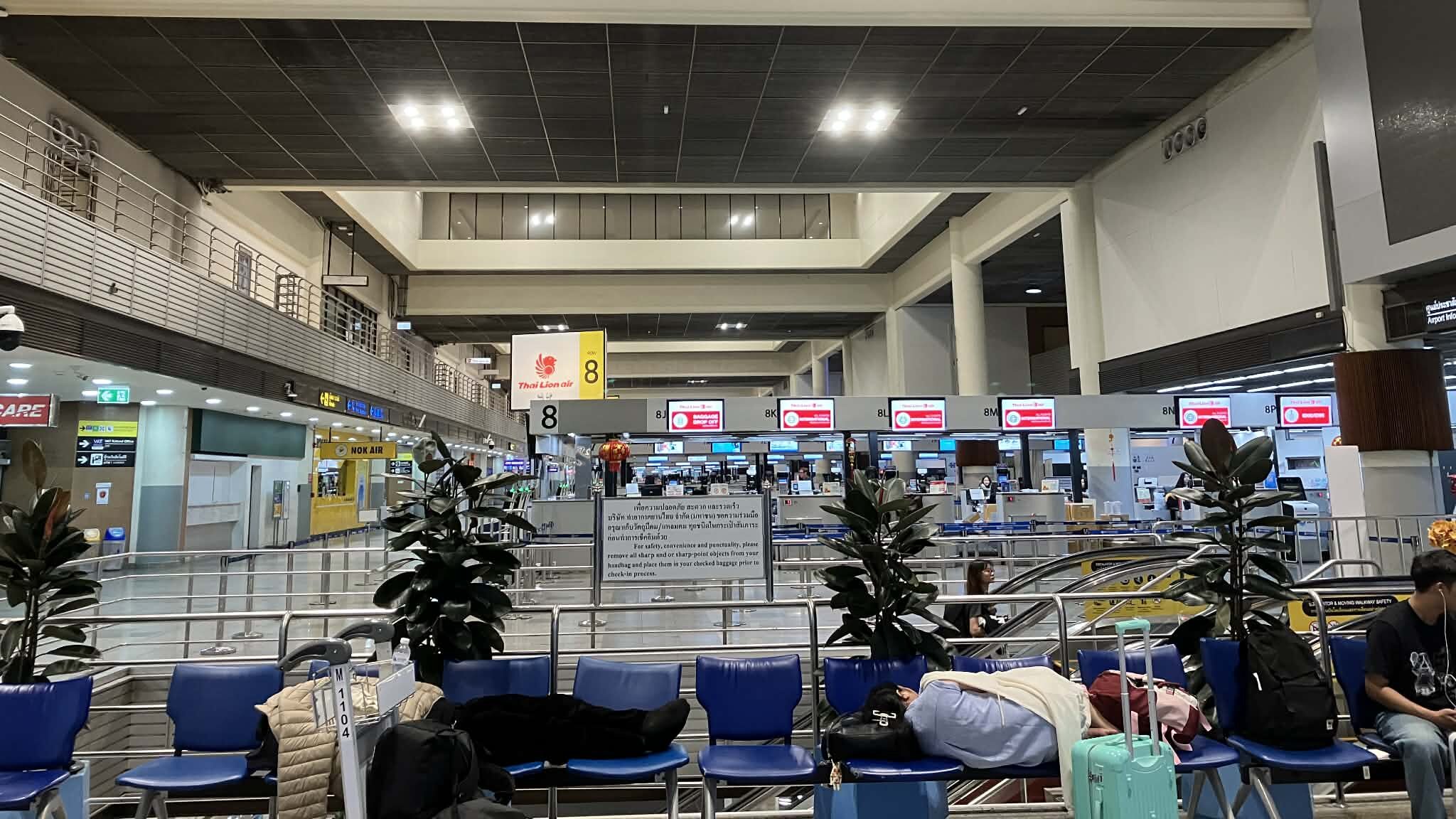 Travelers sleeping on benches overnight at Don Mueang Airport international departure hall